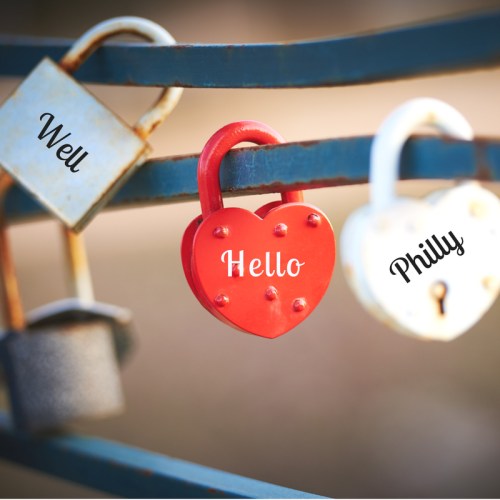 Three padlocks on a fence: one gray, one white, and a red heart-shaped lock with "Hello" and "Philly" written on it.