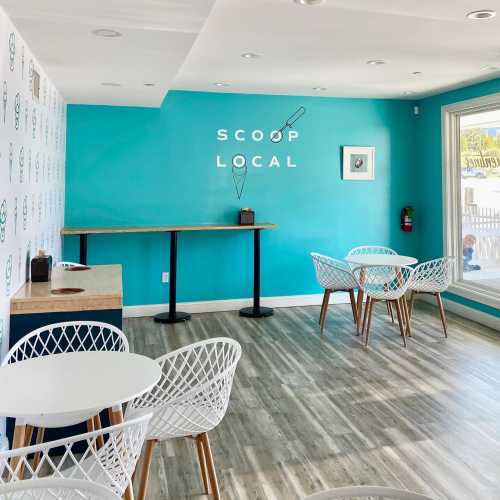 Bright interior of an ice cream shop with turquoise walls, white tables, and modern chairs. "Scoop Local" sign on the wall.