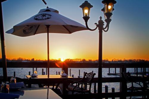A sunset view from a waterfront restaurant, featuring tables, an umbrella, and a lamp by the water.