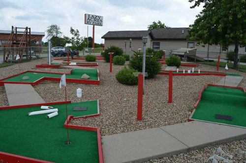 A mini-golf course with red borders, green turf, and obstacles, located at Lazy Acres RV Park.