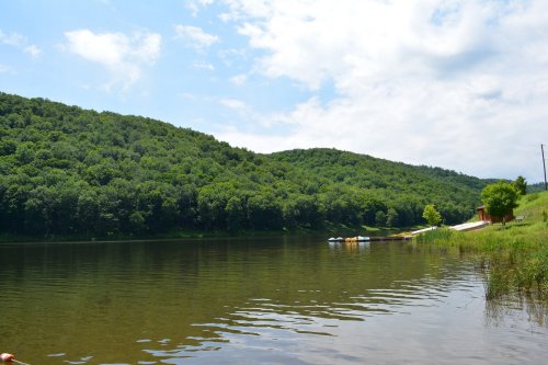 A serene lake surrounded by lush green hills under a partly cloudy sky.