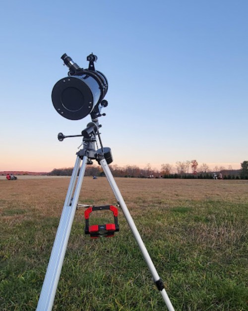 A telescope on a tripod set up in a grassy field during sunset, with a clear blue sky in the background.