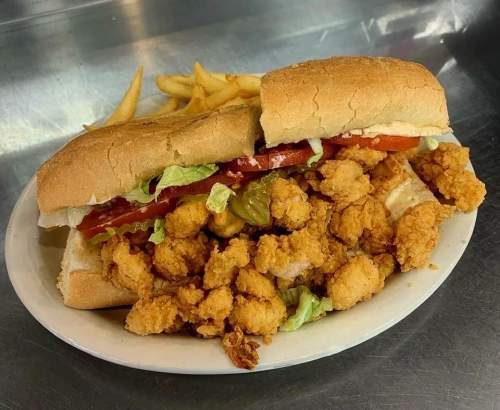 A sandwich filled with fried chicken, lettuce, and tomato, served with a side of fries on a metal tray.