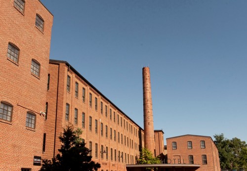 Historic brick factory building with a tall smokestack against a clear blue sky.