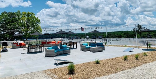 Outdoor patio with colorful seating, umbrellas, and string lights, overlooking a scenic landscape under a blue sky.