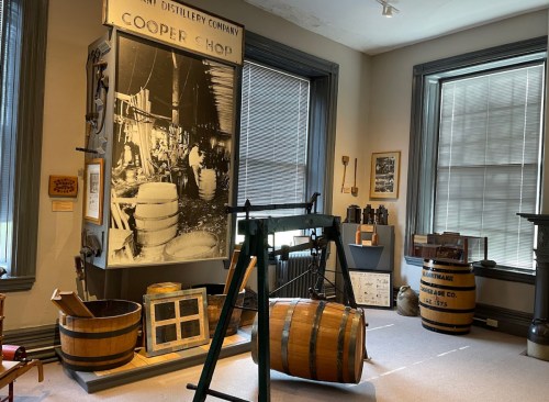 Interior of a distillery museum featuring vintage barrels, tools, and a large historical photo of a cooper shop.