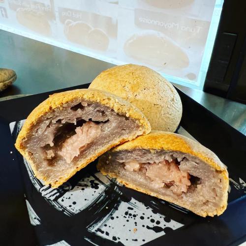 A close-up of a round pastry, cut in half, revealing a pink filling inside a golden-brown crust on a black plate.