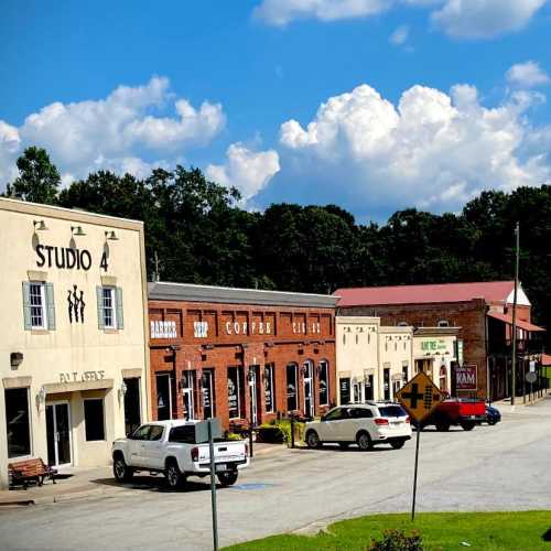 A quaint street with shops, including a studio and coffee shop, under a blue sky with fluffy clouds.