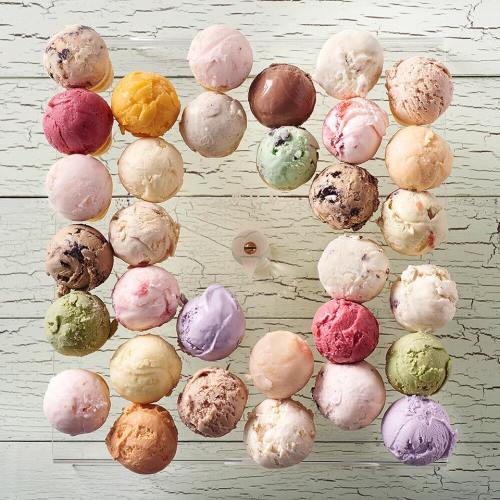 A colorful arrangement of ice cream scoops in various flavors, displayed in a circular pattern on a wooden surface.