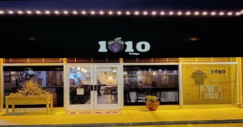 Exterior view of a restaurant named "1010 Bridge," featuring a logo, outdoor seating, and warm lighting at night.