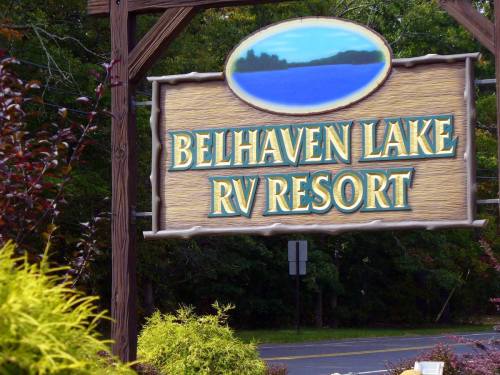 Sign for Belhaven Lake RV Resort, featuring a scenic lake view and surrounded by greenery.