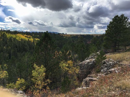 A scenic view of a forested landscape with rocky outcrops, colorful autumn foliage, and dramatic clouds overhead.