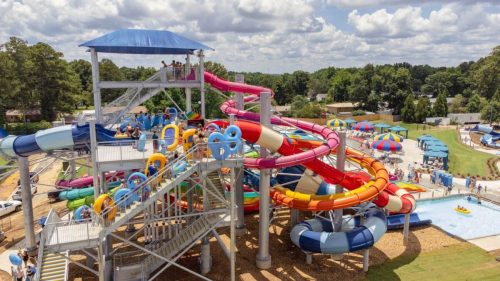 Aerial view of a colorful water park with slides, pools, and people enjoying the attractions on a sunny day.