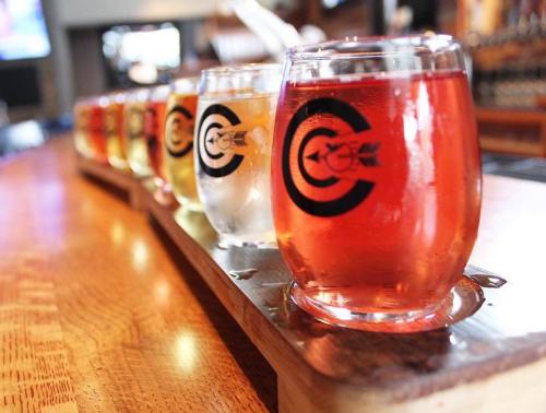 A wooden flight board holds several glasses of colorful craft beers at a bar.