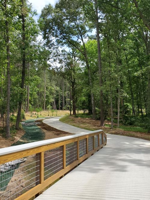 A winding path through a lush green forest, with a wooden railing in the foreground and trees lining the trail.