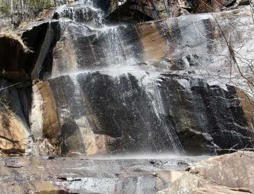 A cascading waterfall flows over rocky cliffs, surrounded by greenery and mist rising from the water.