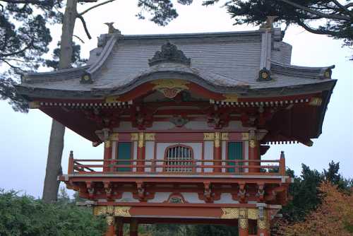 A traditional Japanese pagoda with intricate red and gold detailing, surrounded by trees and a cloudy sky.