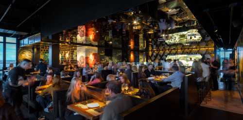 A bustling restaurant interior with diners, stylish decor, and a mirrored ceiling reflecting the vibrant atmosphere.