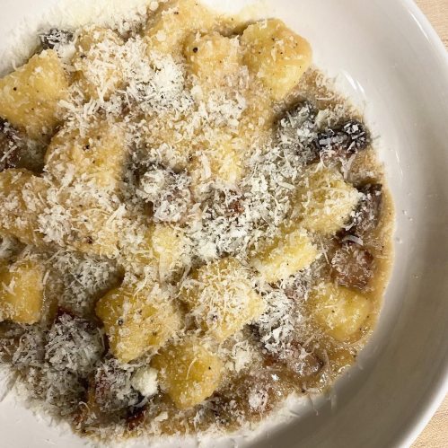 A bowl of gnocchi topped with grated cheese and a savory sauce, garnished with black pepper.