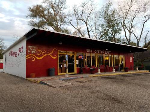 A cozy coffee shop with a red exterior, large windows, and an "Open" sign, surrounded by trees.