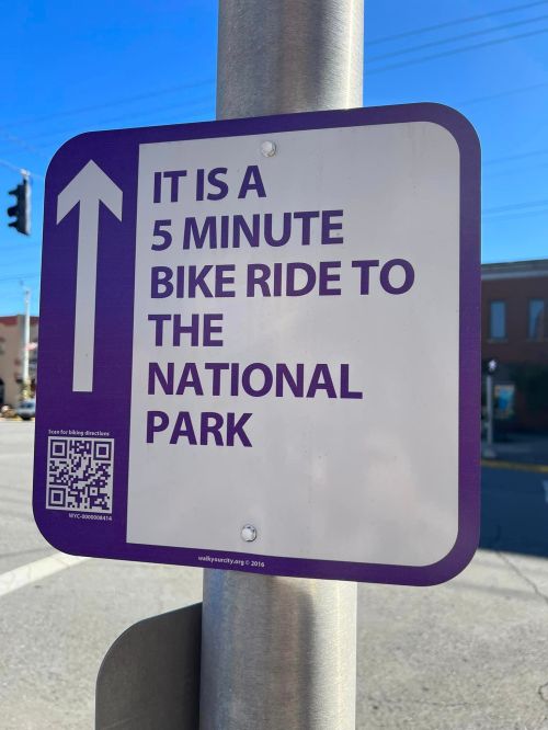 Sign indicating a 5-minute bike ride to the national park, with an arrow and QR code for directions.
