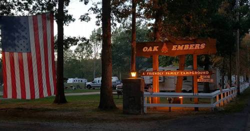 Sign for Oak Embers Campground with an American flag, surrounded by trees and camping trailers in the background.