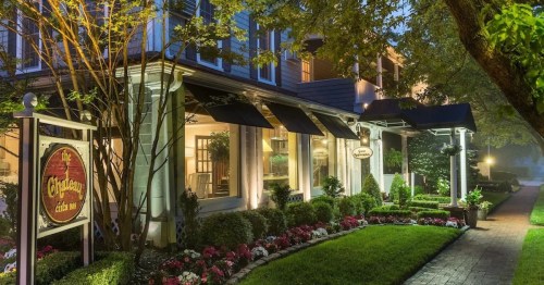 Charming restaurant exterior at dusk, featuring lush gardens, awnings, and a welcoming sign.