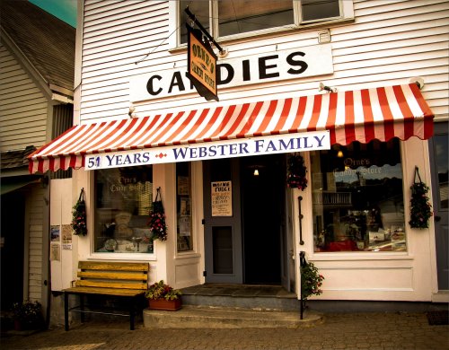 A quaint candy store with a striped awning, celebrating 51 years of the Webster family. Flowers adorn the entrance.