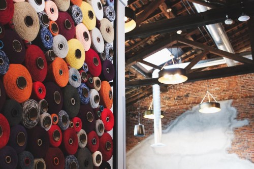 A wall of colorful yarn spools on the left, and a rustic ceiling with pendant lights on the right.