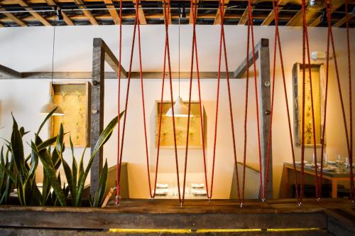 Interior of a modern restaurant featuring wooden beams, plants, and decorative wall art, with red rope accents.
