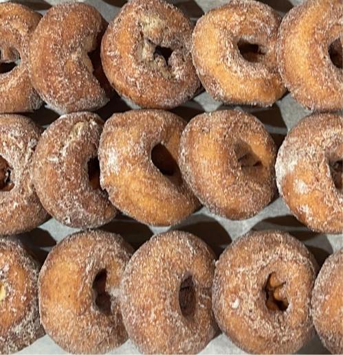 A close-up of freshly made, sugar-coated donuts arranged in a neat row on a tray.