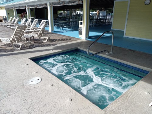 A hot tub with bubbling water, surrounded by lounge chairs and a pool area, under a covered patio.