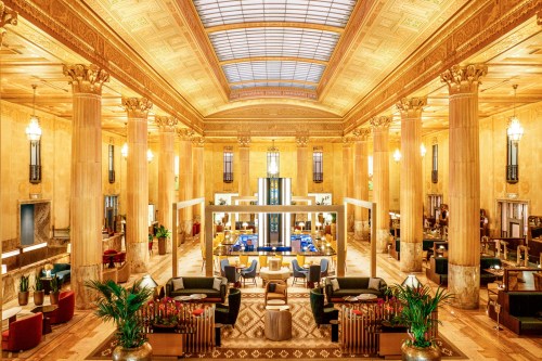 Luxurious hotel lobby with tall columns, elegant decor, and a bright skylight, featuring seating areas and greenery.