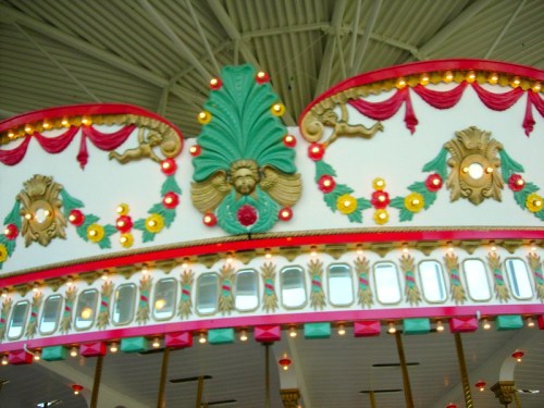 Colorful carousel decoration featuring ornate designs, lights, and floral motifs against a bright ceiling.