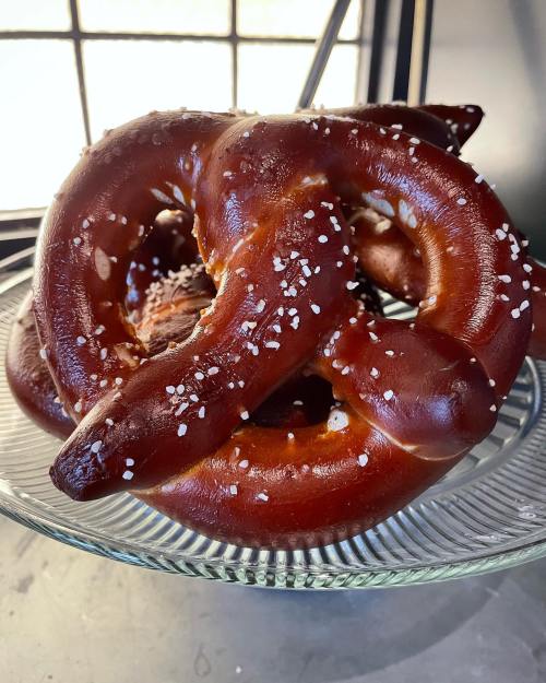 A close-up of freshly baked, golden-brown pretzels sprinkled with coarse salt on a glass plate.