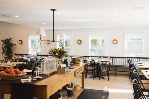 Bright, modern dining area with wooden tables, black chairs, and large windows, featuring a rustic wooden serving table.