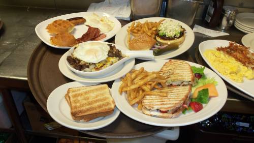 A variety of dishes on a tray, including burgers, waffles, fries, sandwiches, and breakfast items.
