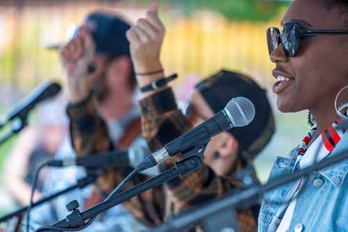 A close-up of musicians performing, with microphones in focus and hands raised in the background, enjoying the music.