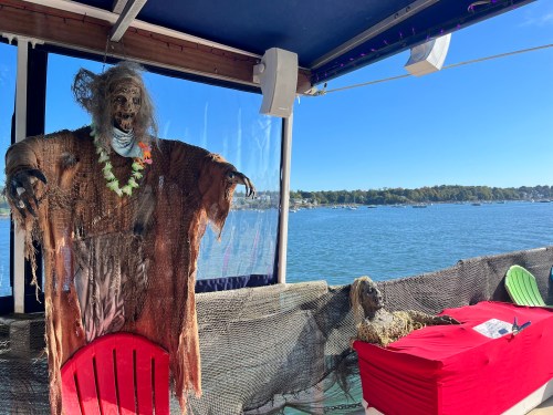 A spooky skeleton decoration in a boat setting, with a view of water and trees in the background.