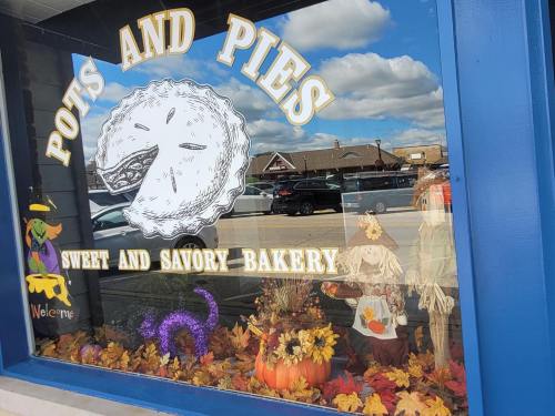 A bakery window display featuring a pie illustration, autumn decorations, and a scarecrow among colorful leaves.