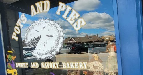 A bakery window display featuring a pie graphic, autumn decorations, and a scarecrow among colorful leaves.