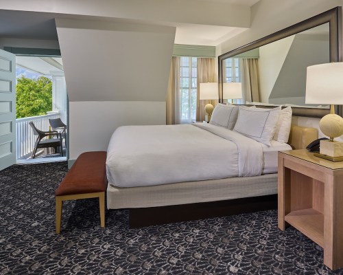 A modern hotel room featuring a king bed, bedside table, and a balcony with natural light.
