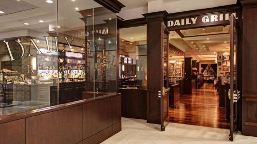 Entrance to the Daily Grill restaurant, featuring a bar area and warm wooden decor.