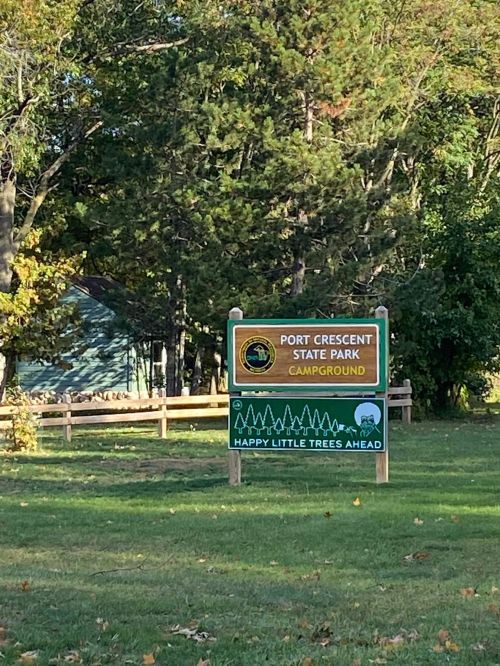 Sign for Port Crescent State Park Campground, featuring trees and a welcoming message about happy little trees ahead.