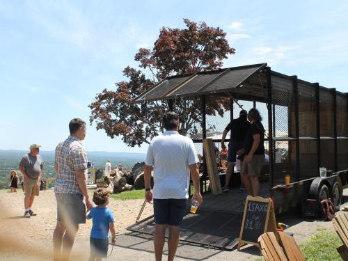A group of people at a food truck on a sunny day, with a scenic view in the background.