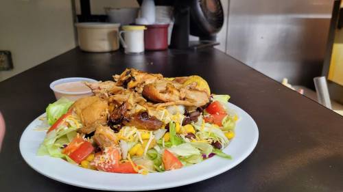 A colorful salad topped with grilled chicken, cheese, and a side of dressing, served on a white plate.