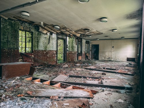 Abandoned room with peeling walls, broken windows, and debris scattered on the floor, creating a desolate atmosphere.