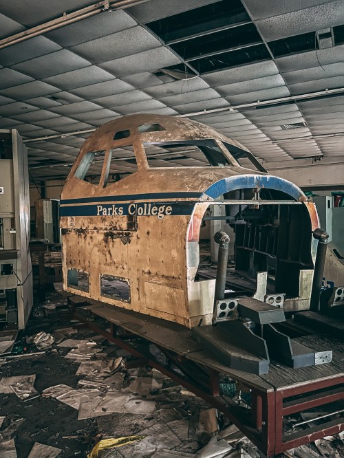 Abandoned aircraft cockpit model in a dusty, cluttered room with scattered papers and peeling paint.