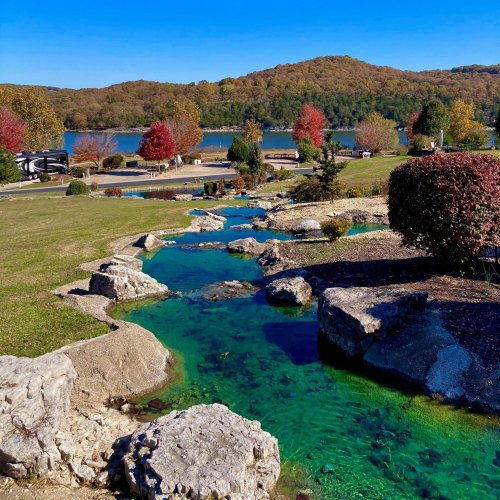 A serene landscape featuring a clear stream, colorful autumn trees, and a lake surrounded by rolling hills.