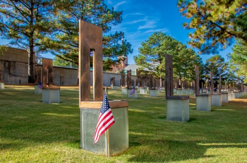 A memorial site featuring empty chairs with American flags, surrounded by trees and a clear blue sky.
